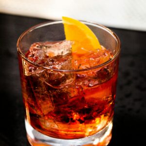 Chilled cocktail with orange slice garnish in a glass on a dark surface.