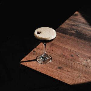 A classic espresso martini cocktail casting a shadow on a rustic wooden table.