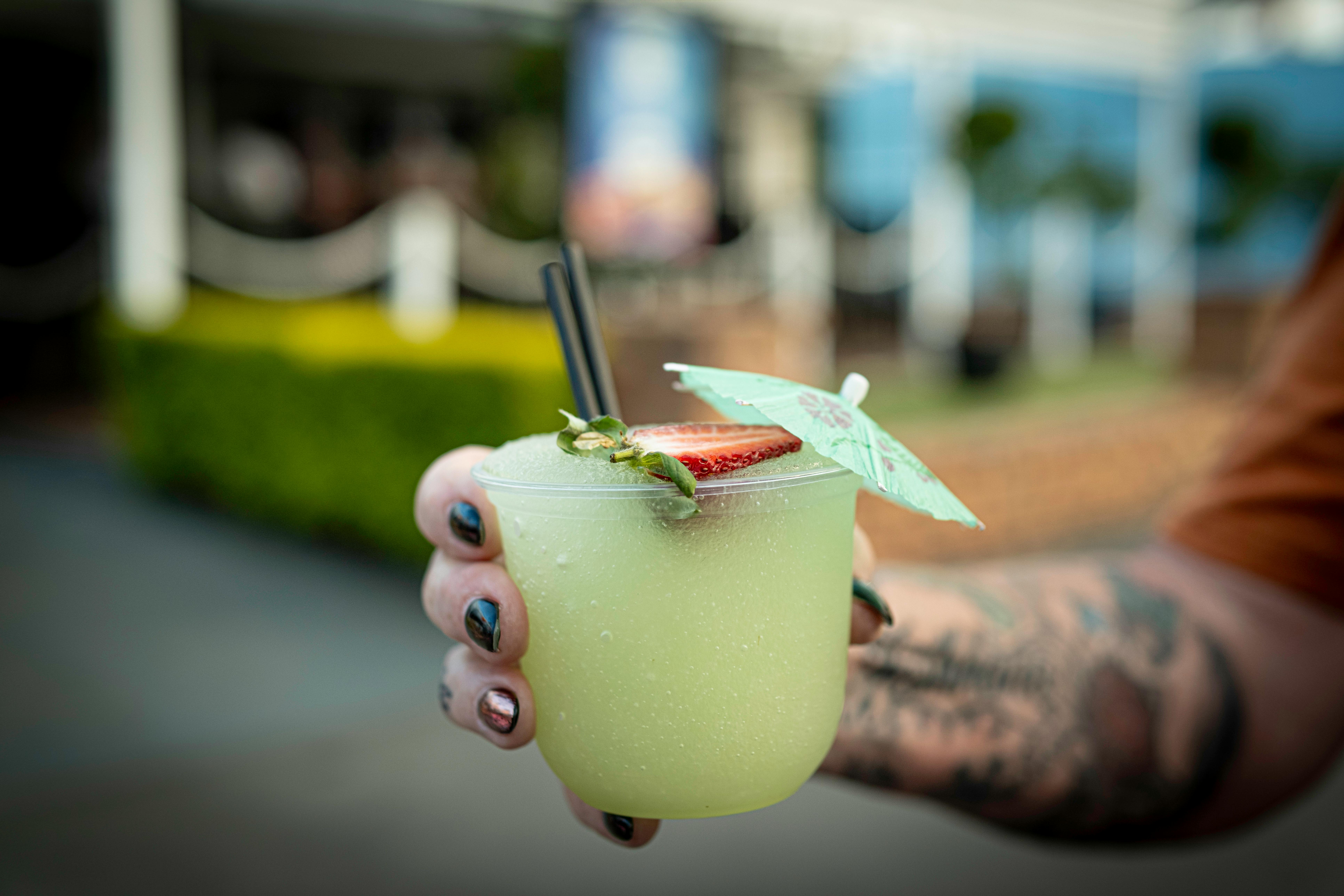 Close-up of a vibrant margarita with a slice of strawberry and umbrella, held outdoors.